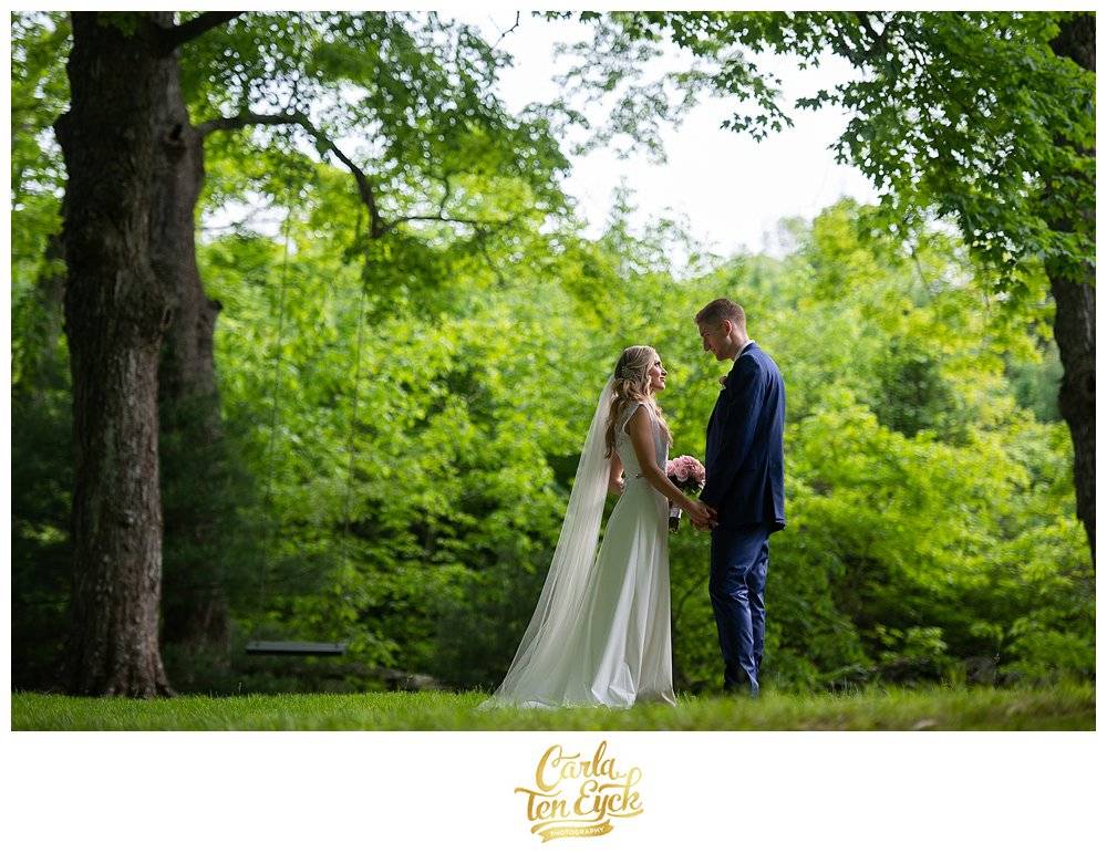 A bride and groom stand in the late afternoon sunlight, newly married, with a swing in the distance at Wright's Mill Farm, Canterbury CT