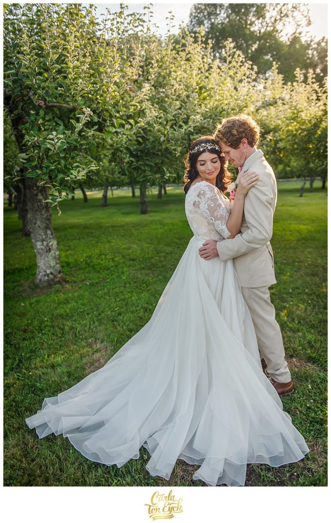 A bride and a groom embrace in an orchard on their wedding day at Smith Farm Garden in East Haddam CT
