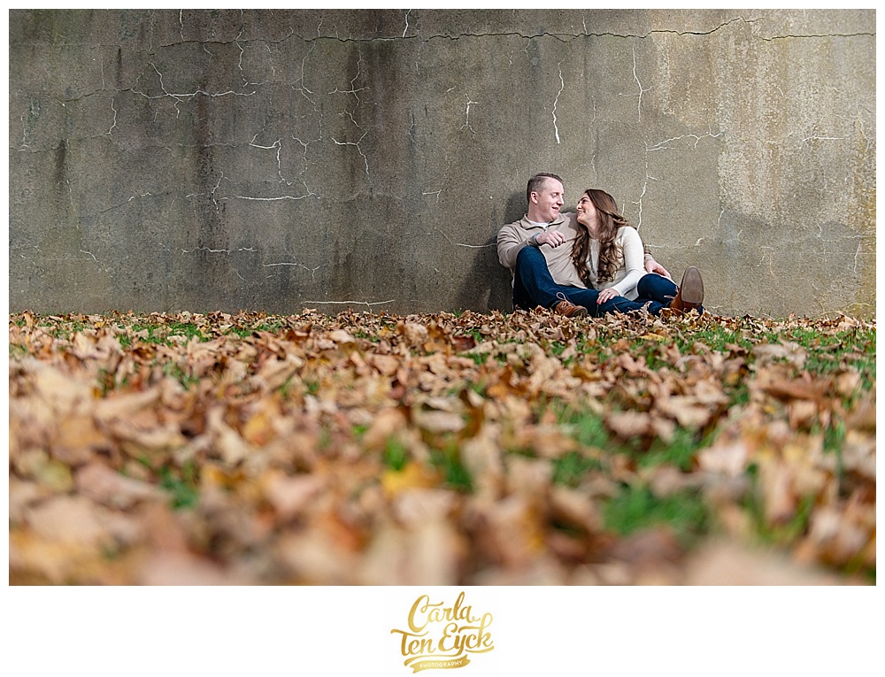 Couple cuddles in the leaves during their autumn engagement session at Harkness Memorial Park in Waterford CT