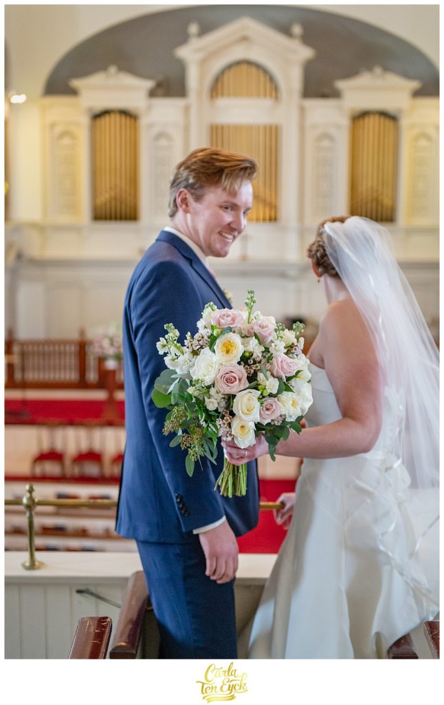 Groom smiles at his bride holding a white and pink rose wedding bouquet at First Congregational church in Danbury CT