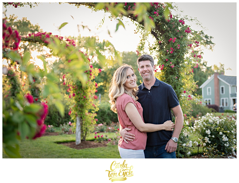 Couple smiles under the rose arches in the rose garden in Hartford CT at Elizabeth Park