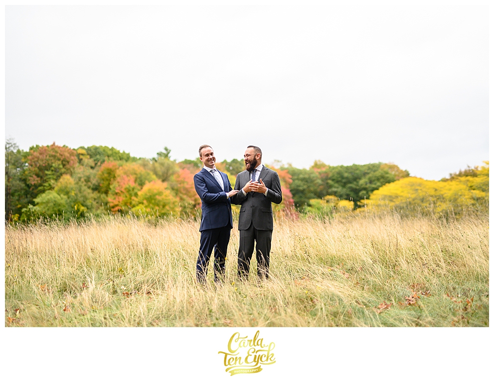 Two grooms laugh in a field at their wedding at the Eustis Estate in Milton MA