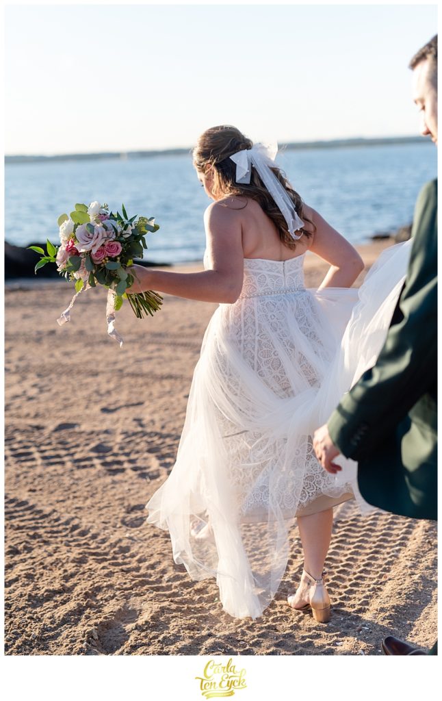A bride and groom pose for pictures on the beach after their wedding at Lighthouse Point Park in New Haven CT