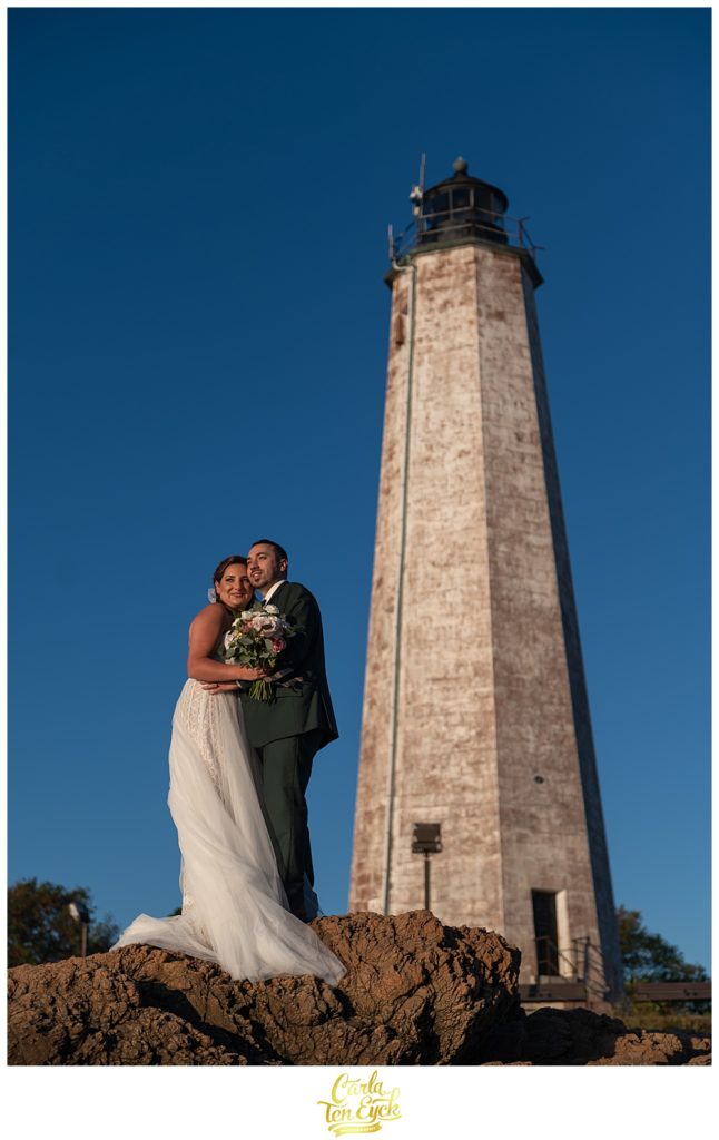 A bride and groom pose for pictures on the beach by the lighthouse after their wedding at Lighthouse Point Park in New Haven CT
