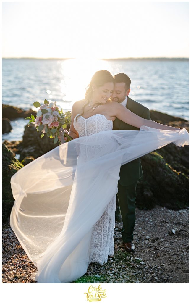 A bride and groom pose for pictures on the beach after their wedding at Lighthouse Point Park in New Haven CT
