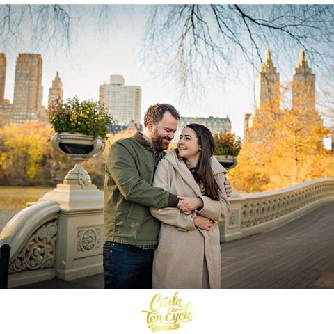 A couple embraces on a desserted bridge during their engagement session in Central Park NYC during Covid