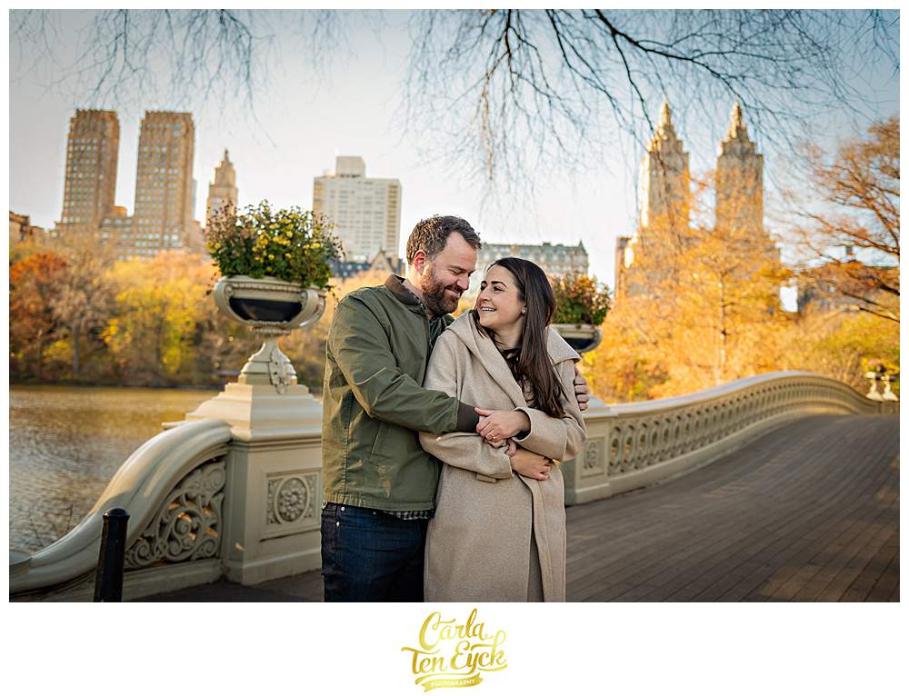 A couple embraces on a desserted bridge during their engagement session in Central Park NYC during Covid