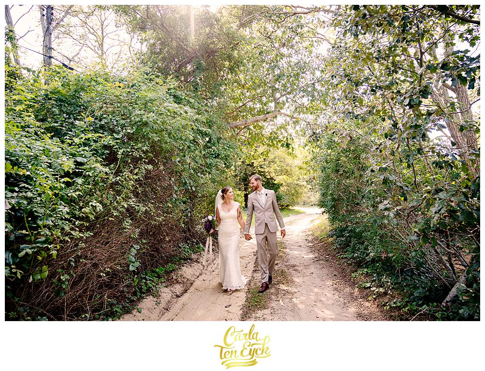 A bride and groom walk on a sandy path at their Wellfleet Preservation Hall wedding on Cape Cod MA