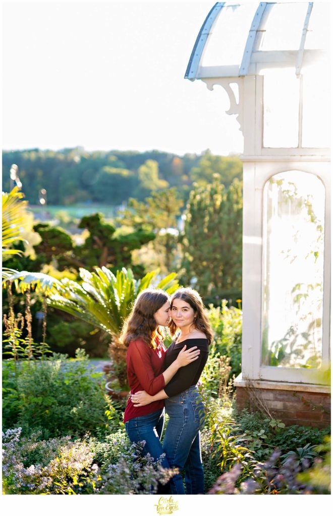 Two brides to be snuggle at the Smith College conservatory in Northampton MA during their engagement session.