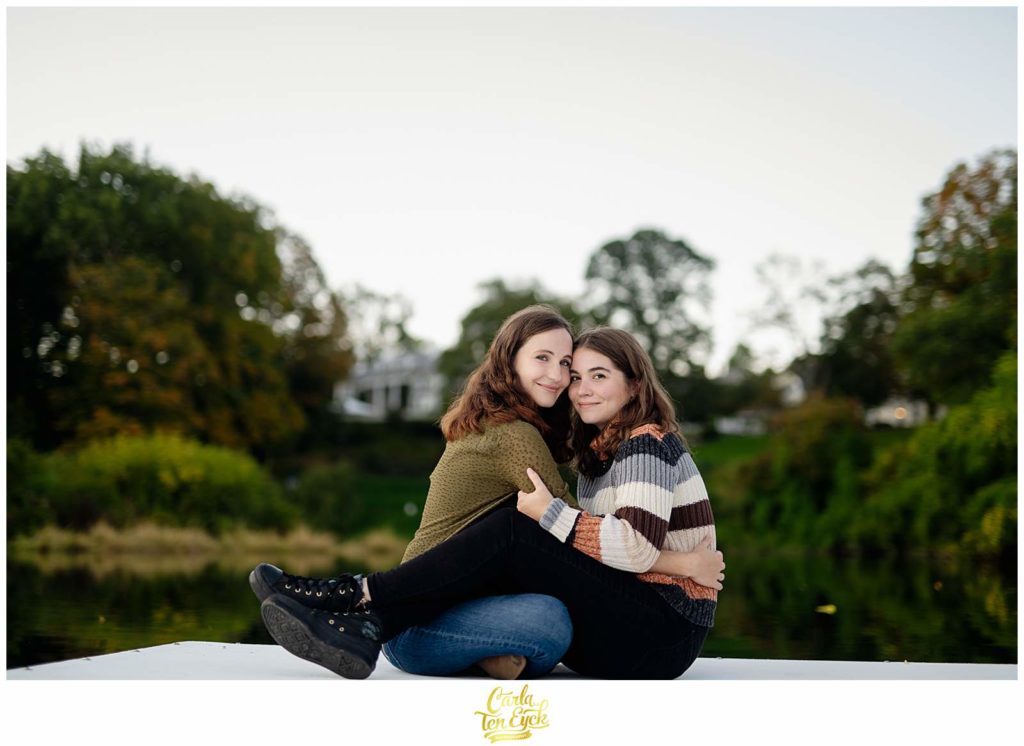Two brides snuggle on the dock at the boat house on the Smith College campus in Northampton MA during their engagement session.