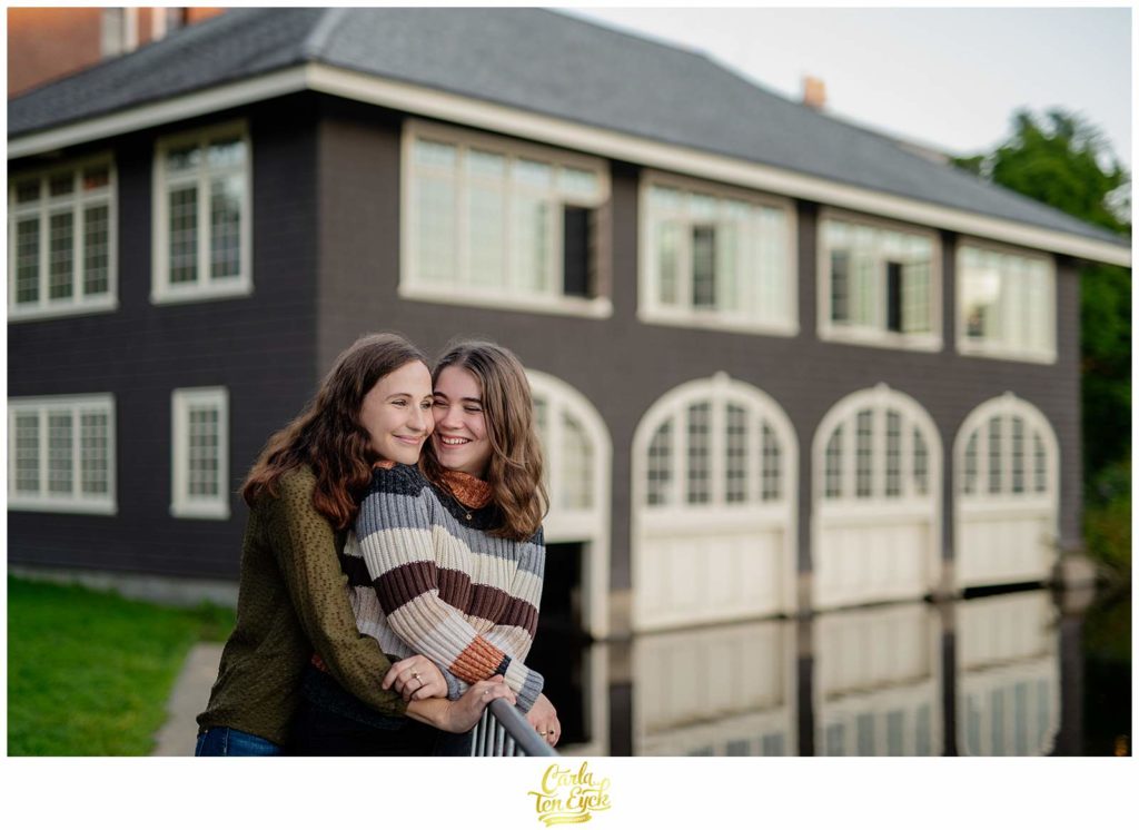 Two brides snuggle at the boat house during their engagement session on the Smith college campus in Northampton MA
