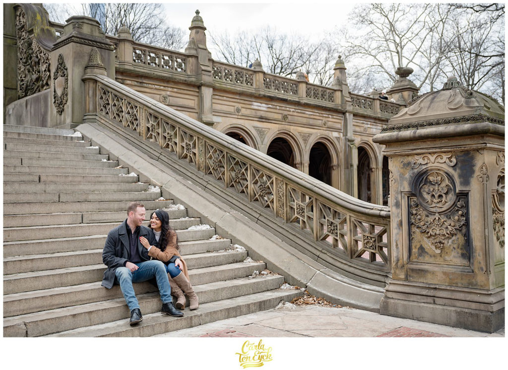 A couple cuddles by the stunning and iconic Bethesda Fountain in Central Park during their winter engagement session