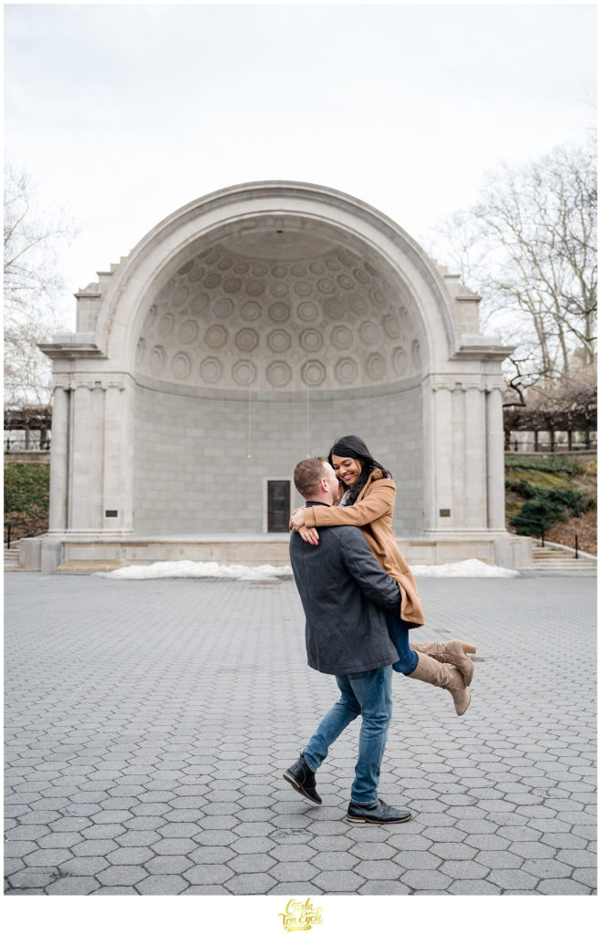 A couple dances in front of the iconic bandshell in Central Park during their winter engagement session 