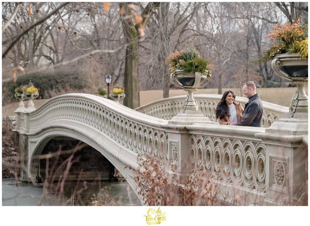 A couple cuddles on the iconic Bow Bridge during their winter engagement session in Central Park NYC
