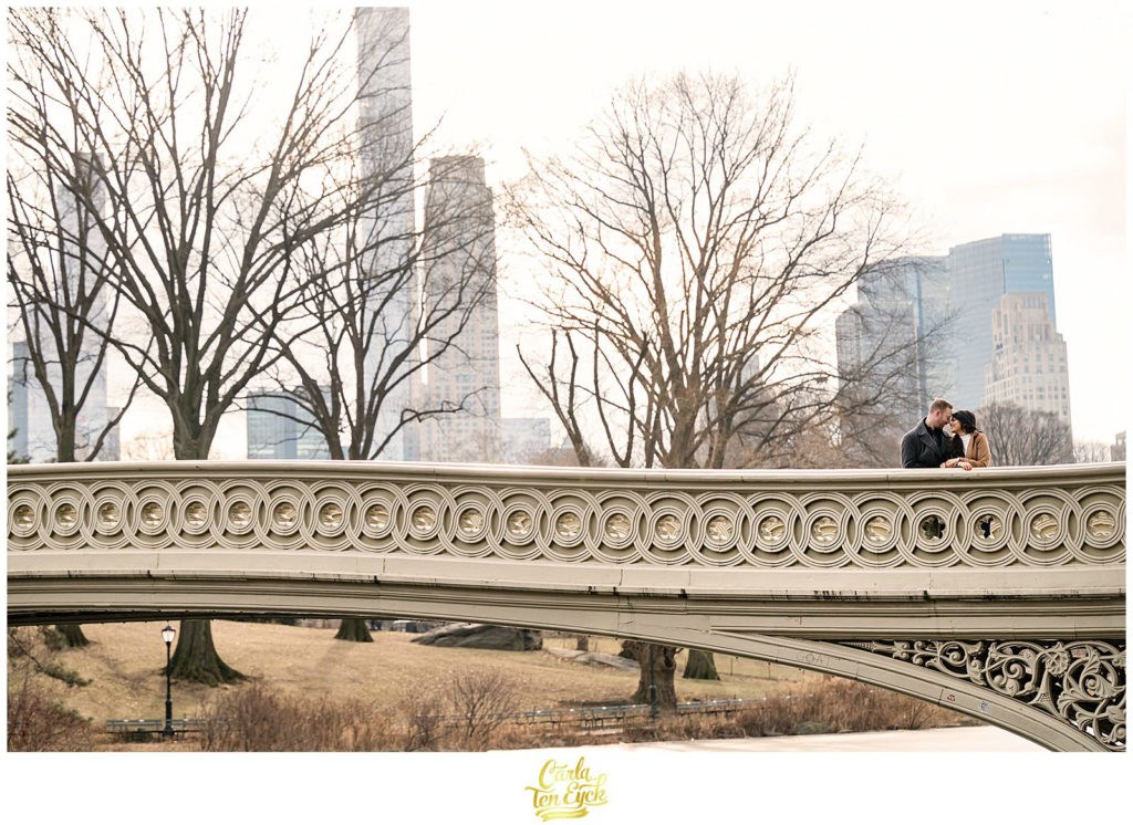 A couple kisses on the iconic Bow Bridge during their winter engagement session in Central Park NYC