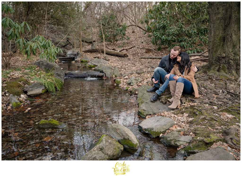 A couple snuggles by a creek in The Ramble during their winter engagement session in Central Park