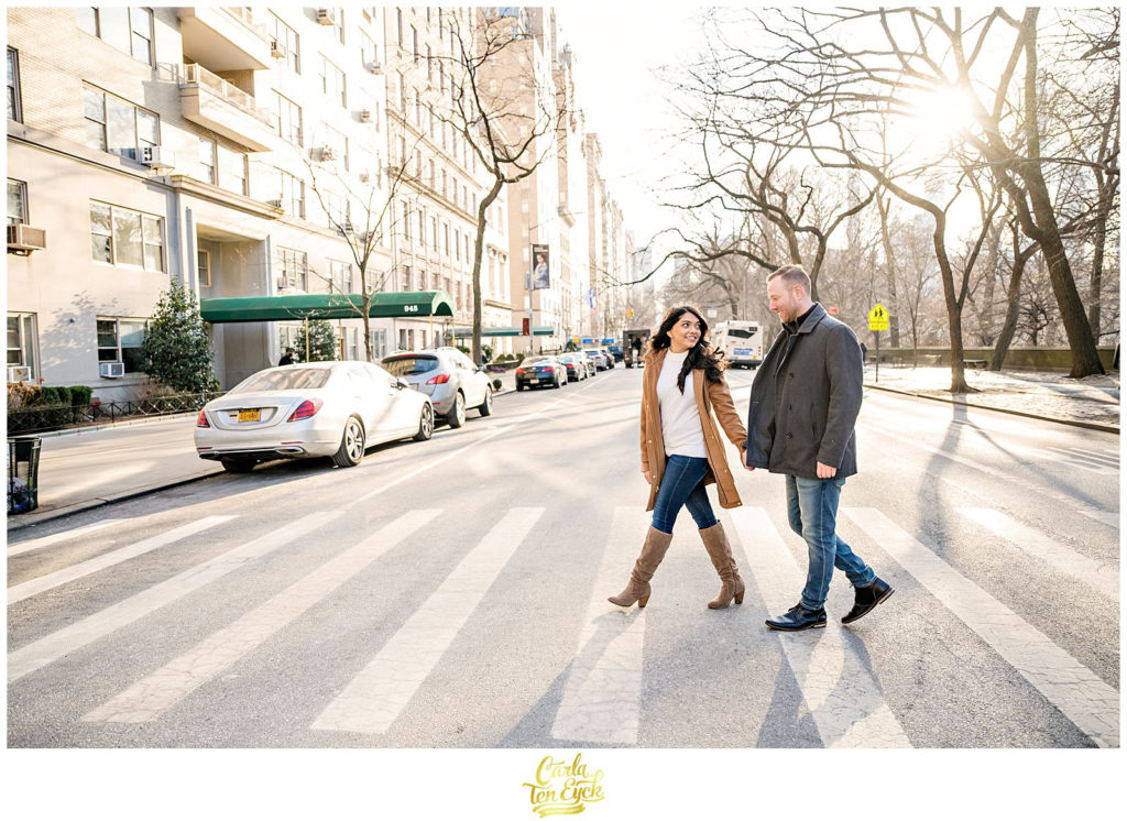 A couple walks across the street in Central Park NYC for their engagement session 