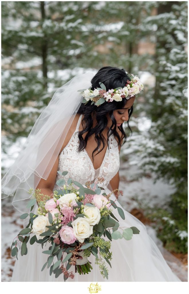 A bride with her flower crown stands in the snowy woods for her wedding at The Pavilion at Crystal Lake in Middletown, CT