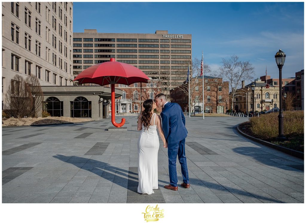A bride and groom kiss by the Travelers umbrella in downtown Hartford at their Hartford City Hall Spring elopement, in Hartford CT